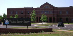 Photo of the brown brick front of the Shared Services Center building, including its sign and parking lot, located in Sandersville, Georgia.